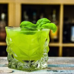 Green mixed drink with mint leaves in a clear square looking glass
