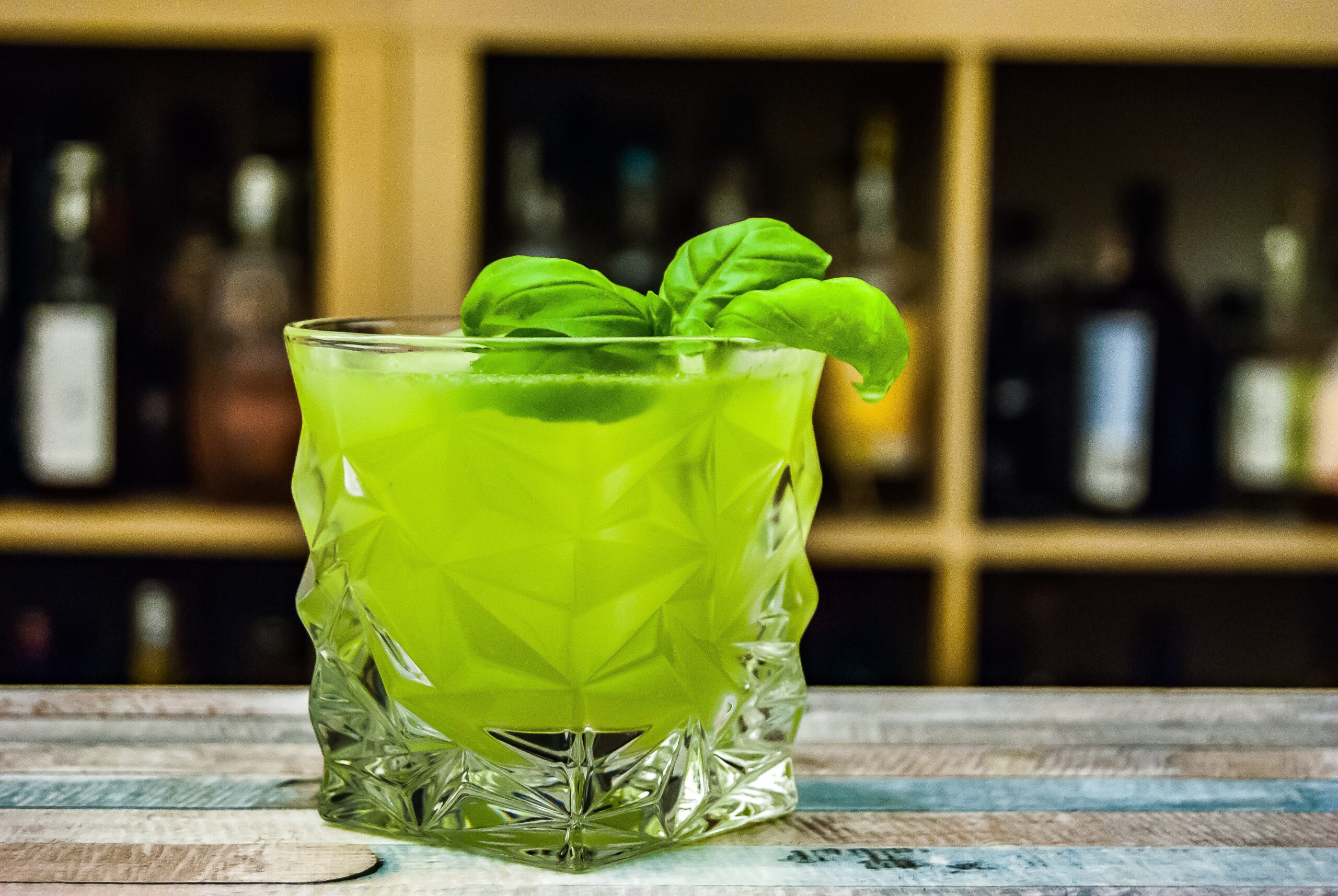 Green mixed drink with mint leaves in a clear square looking glass